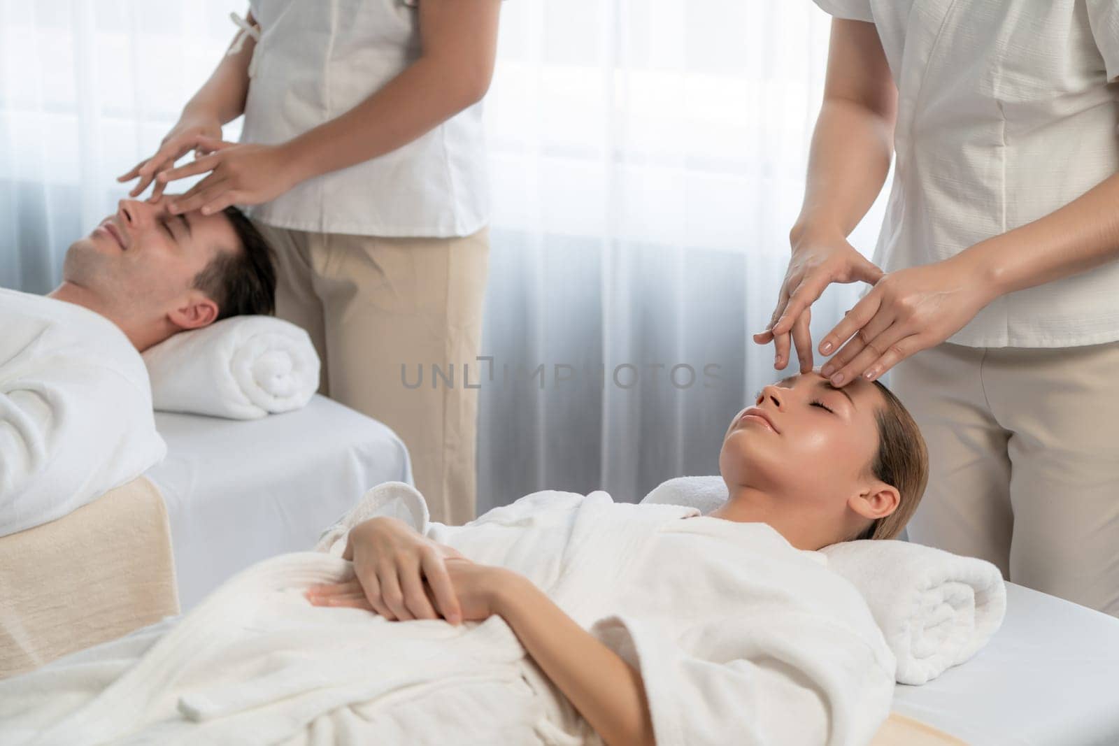 Caucasian couple enjoying relaxing anti-stress head massage and pampering facial beauty skin recreation leisure in dayspa modern light ambient at luxury resort or hotel spa salon. Quiescent