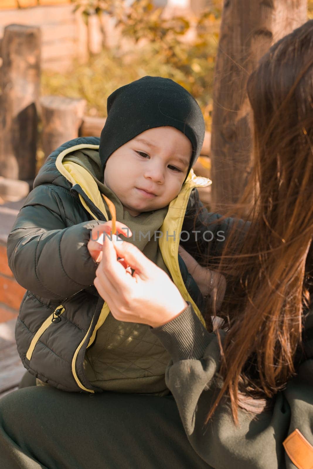 Cute little boy stands with mother outdoors. Happy child walking in autumn park. Toddler baby boy wears trendy jacket and hat. Autumn fashion. Stylish child outside