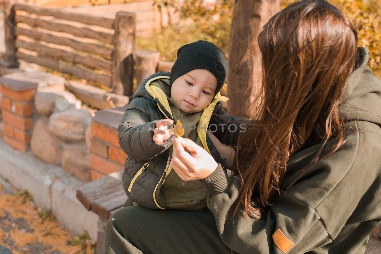 Cute little boy stands with mother outdoors. Happy child walking in autumn park. Toddler baby boy wears trendy jacket and hat. Autumn fashion. Stylish child outside
