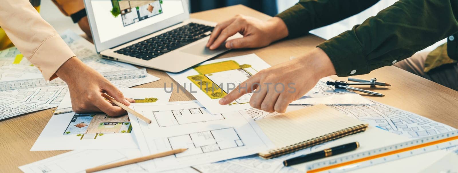 Professional architect shows mistake structure in blueprint while analysis and comparison with picture in laptop on table with blueprint and architectural equipment. Cropped image. Delineation.