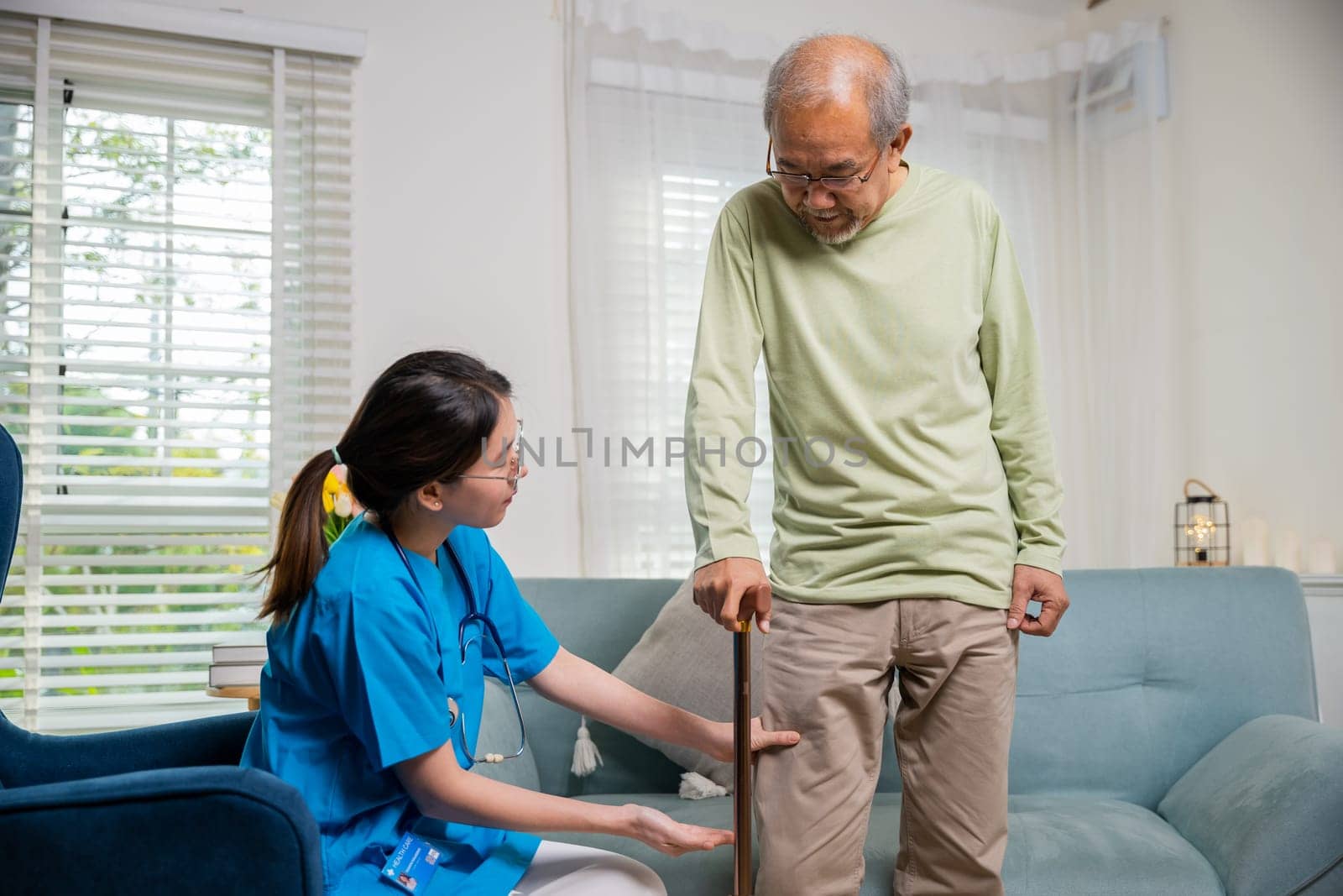 Asian young woman nurse checking knee and leg after surgery of senior old man patient suffering from pain in knee, doctor asking elderly man about pain symptom with walking stick