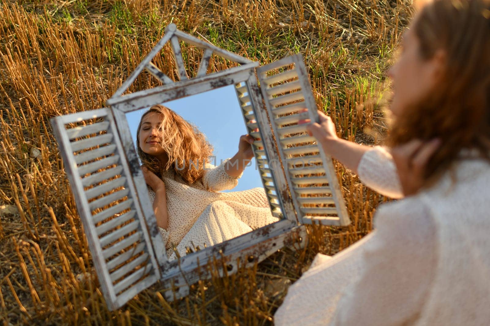 Woman looking into a mirror in a wheat field at a sunset