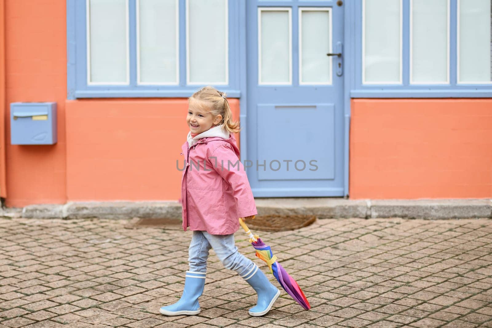 A girl in rubber boots and an umbrella is walking on the pavement