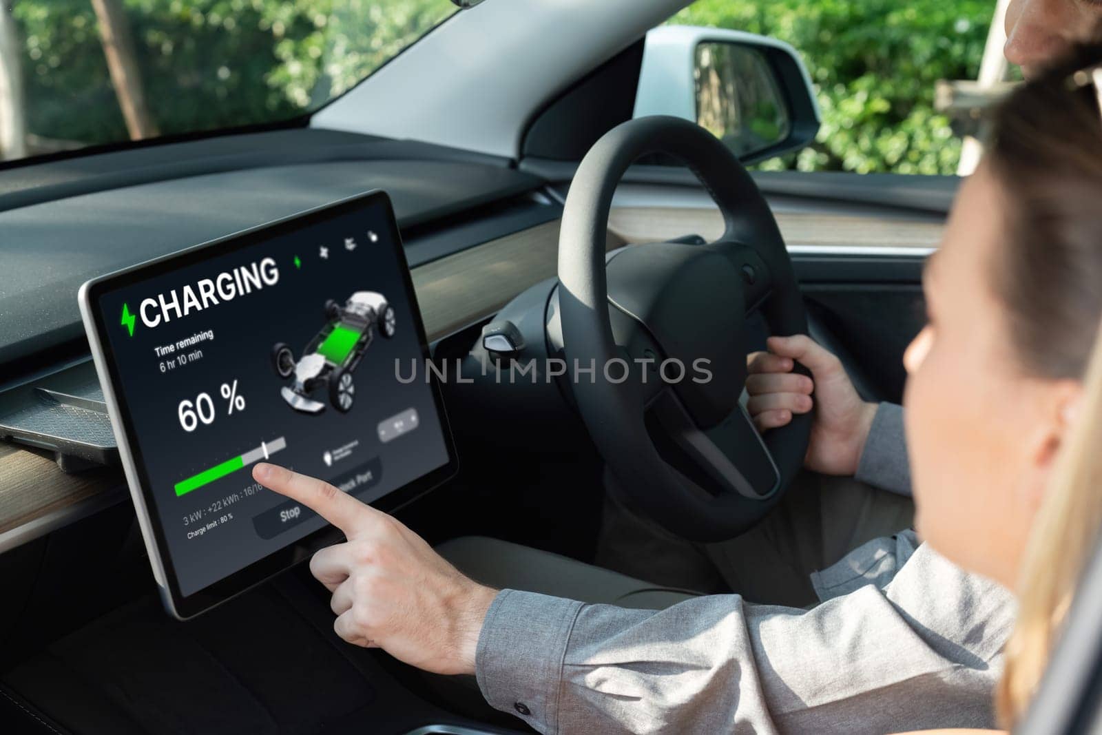 Electric car driver checks battery charging status, range and charging limit on app screen in the car. Smart technology device show EV car recharging data of electric storage in car battery innards.