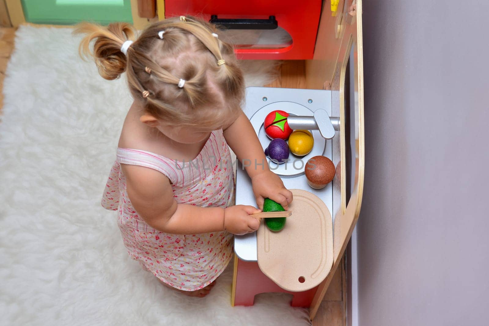 Girl cuts wooden vegetables on toy kitchen wooden cooking toy.
