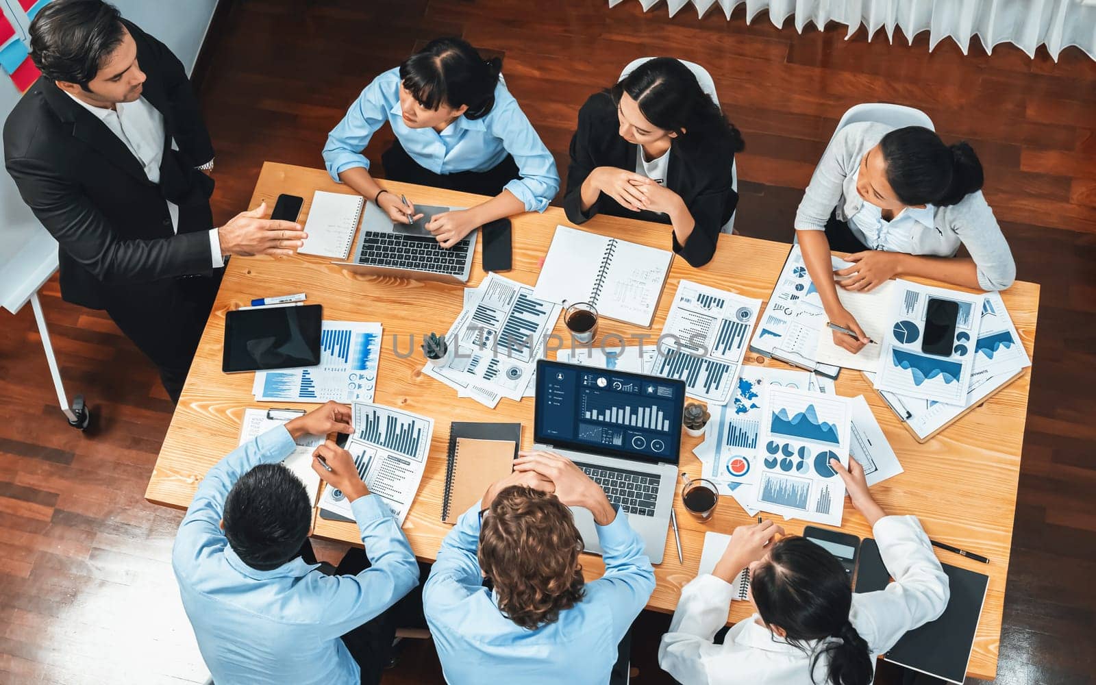 Wide top view of diverse group of business analyst team analyzing financial data report paper on meeting table. Chart and graph dashboard by business intelligence analysis. Meticulous