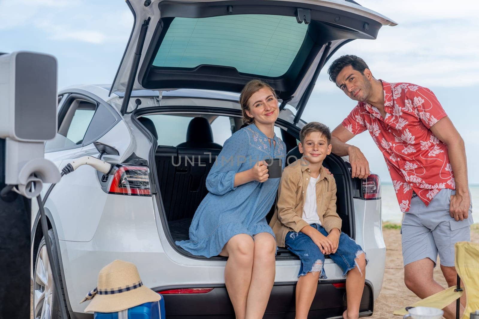 Family vacation trip traveling by the beach with electric car, happy family recharge EV car, enjoying outdoor camping coffee. Seascape travel and eco-friendly car for clean environment. Perpetual