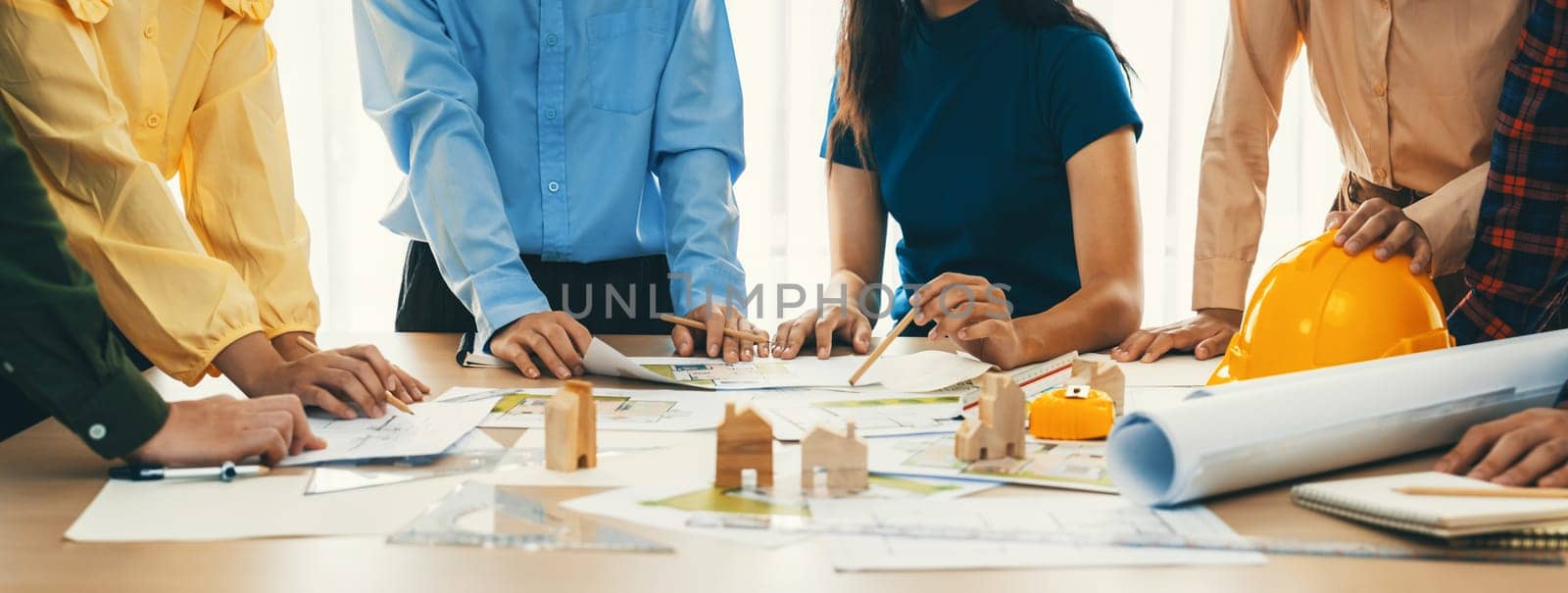 Professional architect engineer team discussion about architectural project on meeting table with wooden block and blueprint scatter around. Design and cooperate concept. Closeup. Delineation.