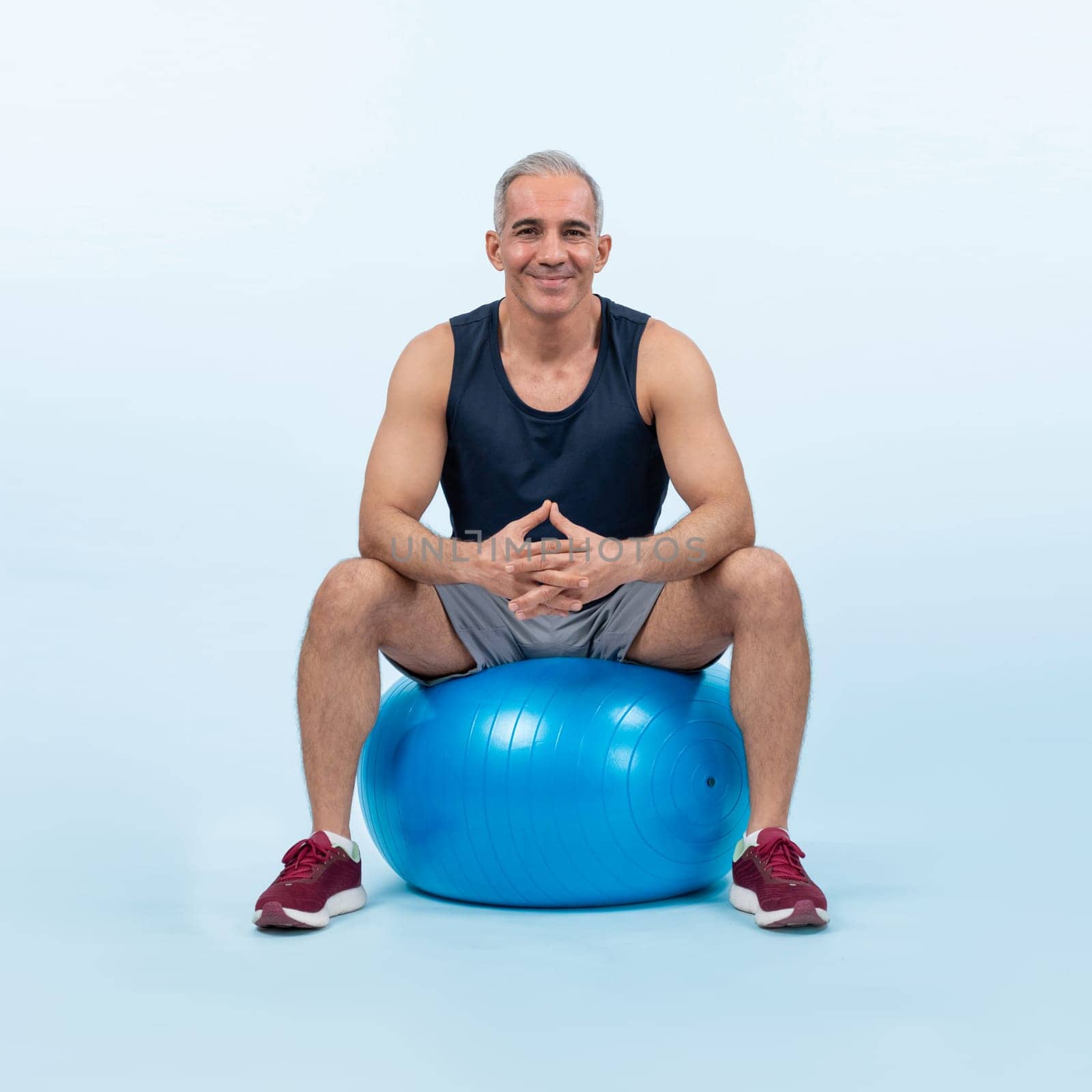 Full body length shot athletic and sporty senior man with fitness exercising ball in sitting posture on isolated background. Healthy active and body care lifestyle after retirement. Clout