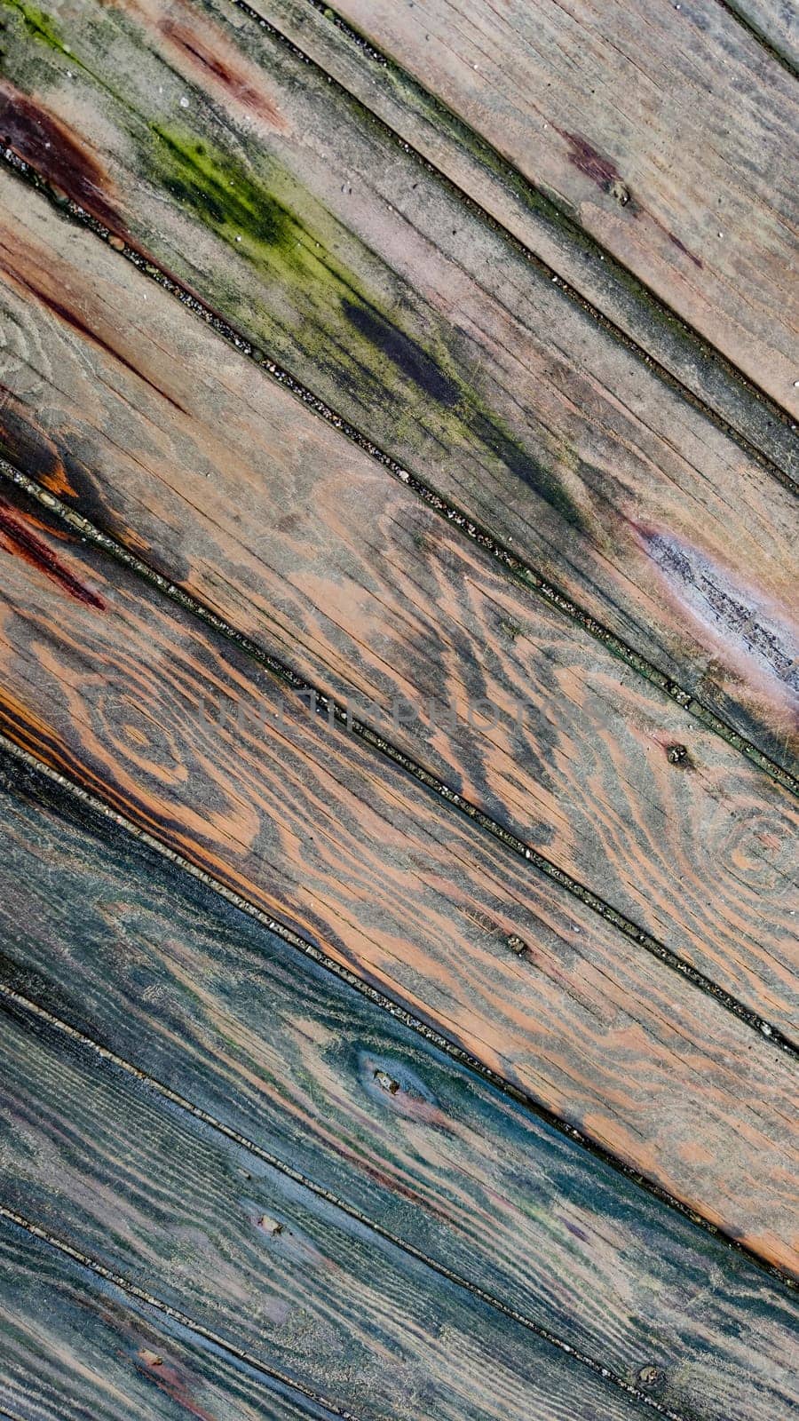 Background of textured wooden surface made of boards with multicolored spots from humidity, diagonal lines, top view, close-up.