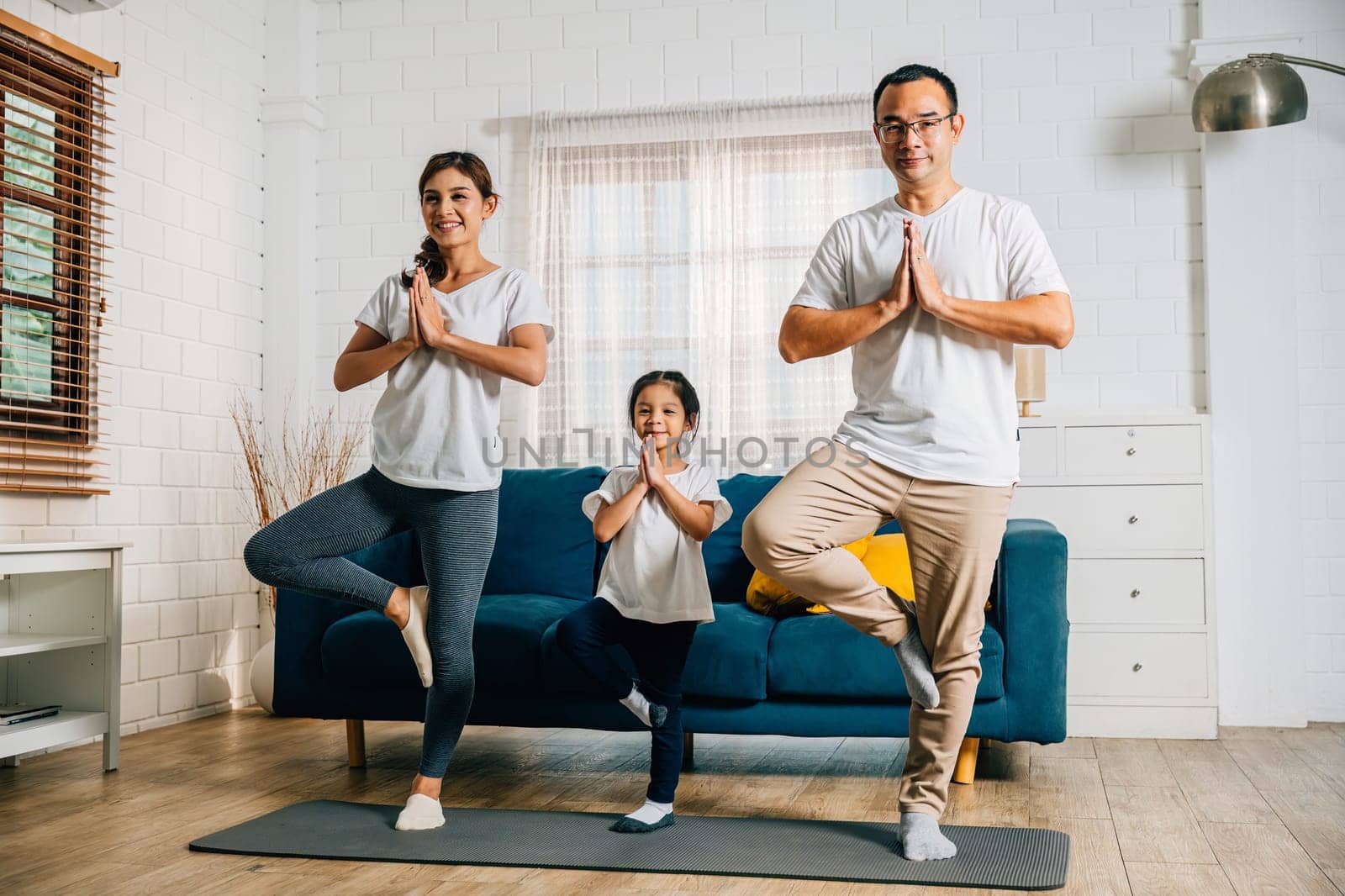 Asian parents and their daughter practice yoga and fitness training on the living room floor by Sorapop