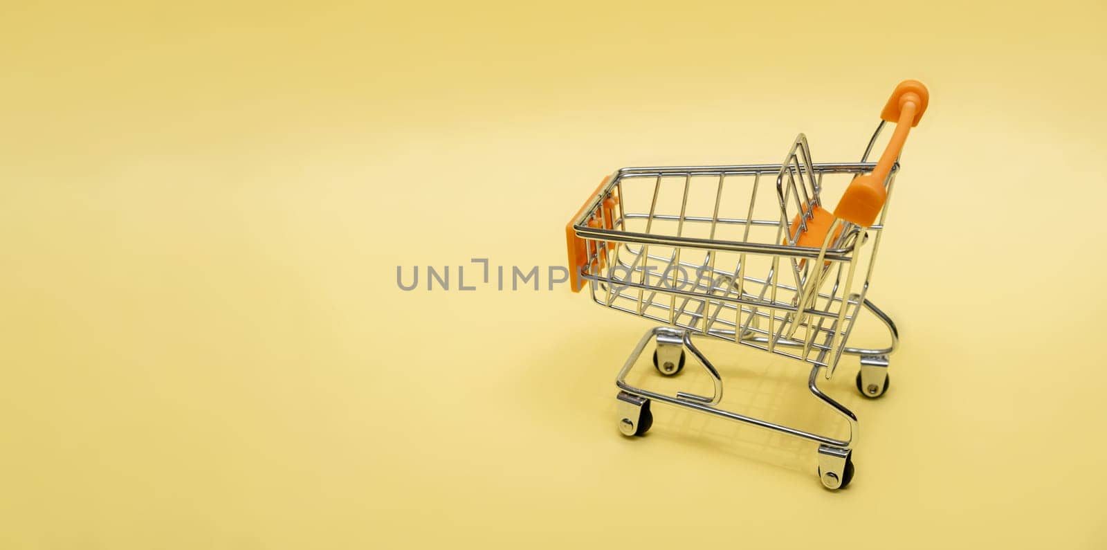 Small cart on a yellow background. Small supermarket grocery push cart for shopping. Shopaholic. Buyer. Shopping concept. Close-up. Isolated shopping trolley on a yellow background. Copy space.