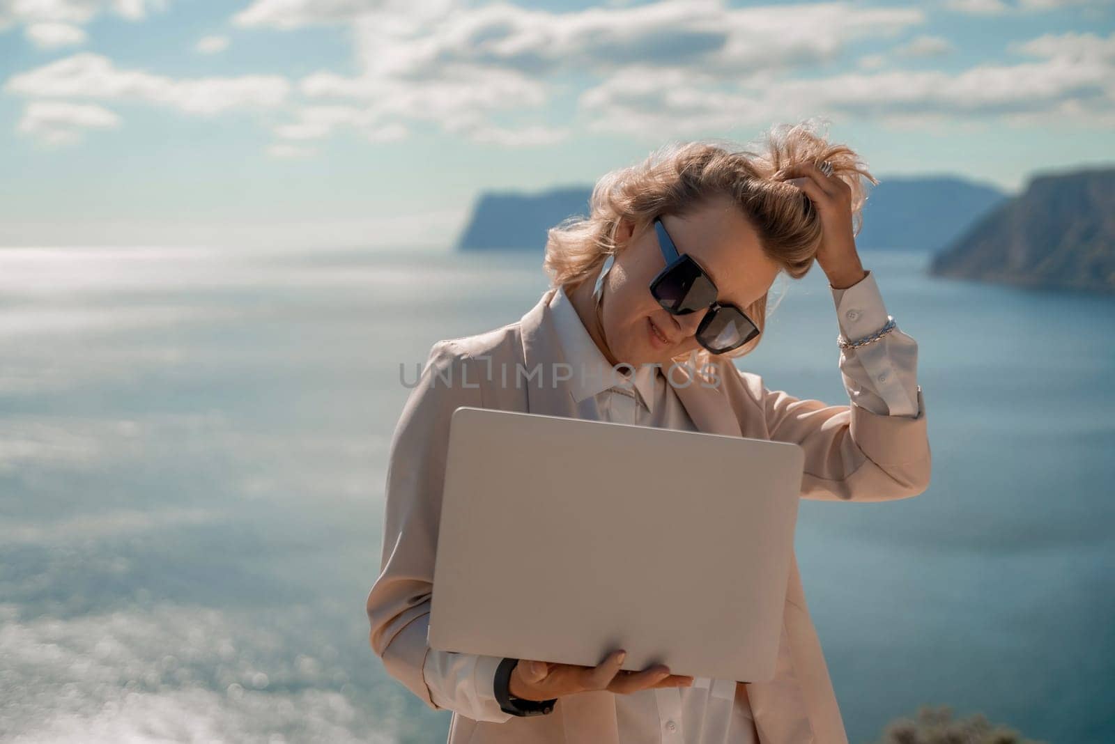 Freelance women sea. She is working on the computer. Good looking middle aged woman typing on a laptop keyboard outdoors with a beautiful sea view. The concept of remote work