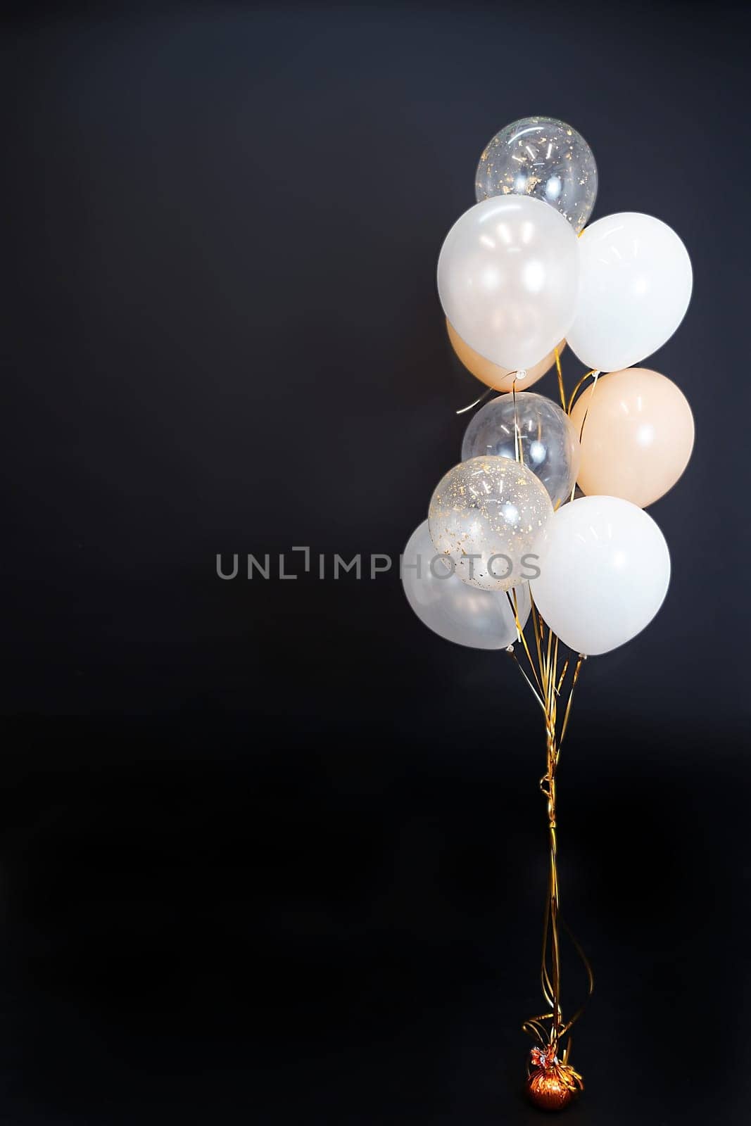 On a black background, balloons of light shades - white, beige, transparent - are flying. Space for text. High quality photo