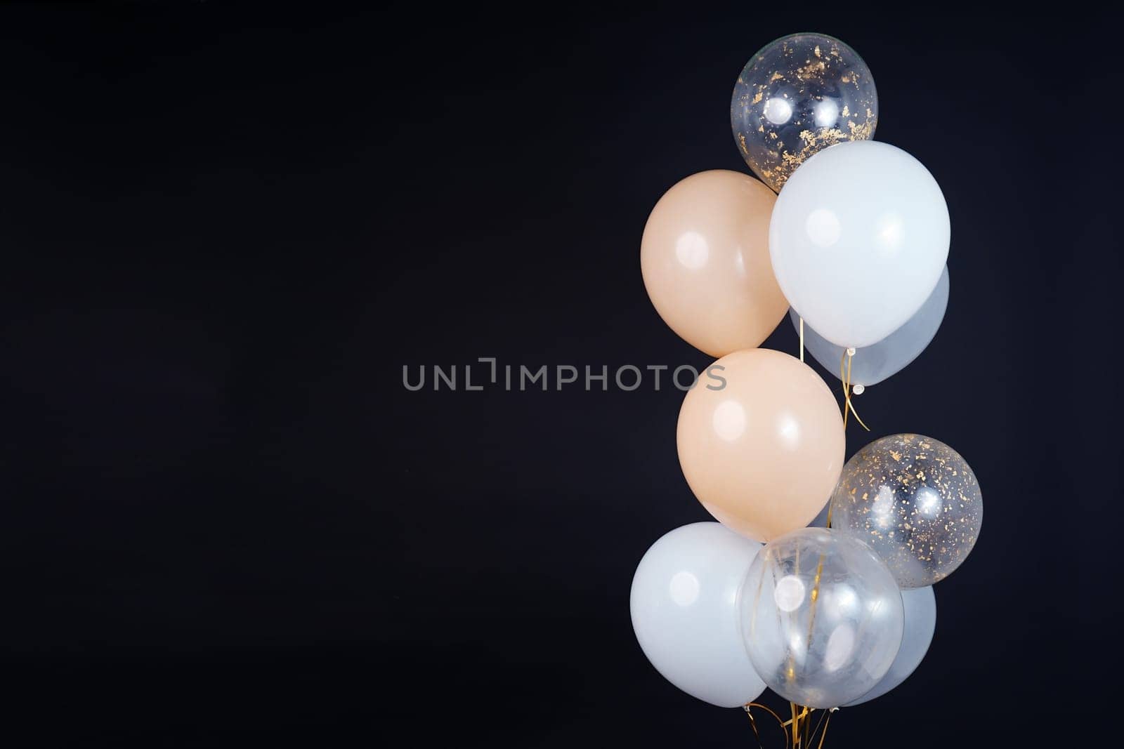 A bunch of balloons in white, beige and transparent colors on a dark background with space for an inscription. High quality photo