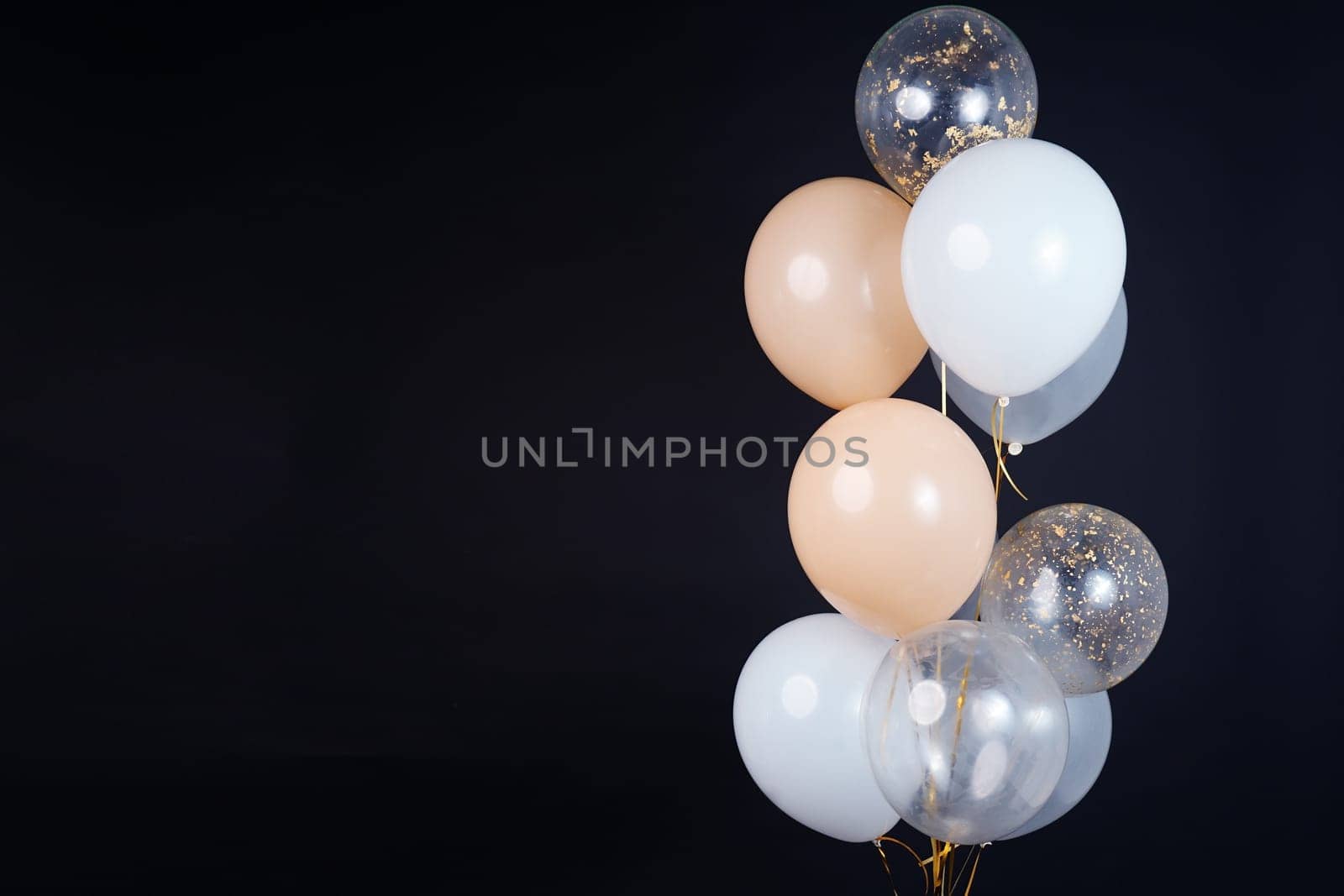 A bunch of balloons in white, beige and transparent colors on a dark background with space for an inscription. High quality photo