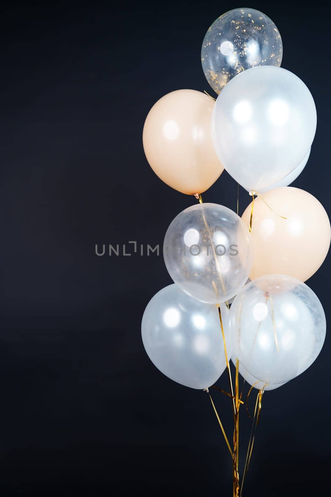 A bunch of balloons in white, beige and transparent colors on a dark background with space for an inscription. High quality photo