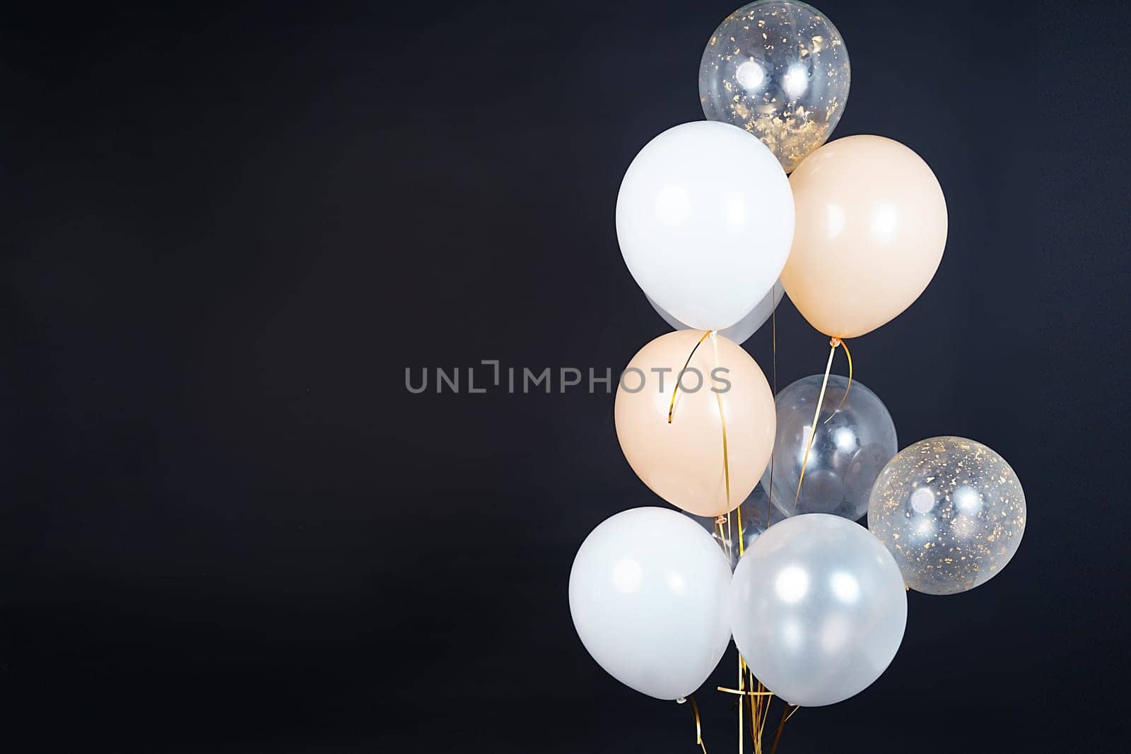 A bunch of balloons in white, beige and transparent colors on a dark background with space for an inscription. High quality photo