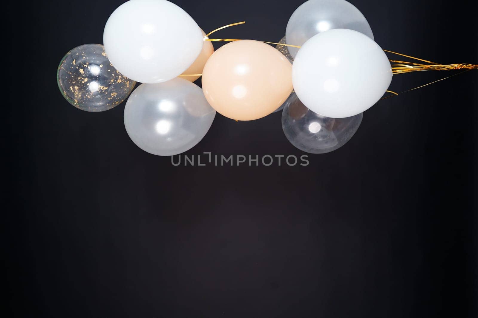 On a black background, balloons of light shades - white, beige, transparent - are flying. Space for text. High quality photo