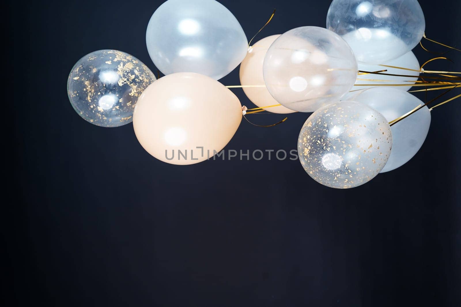 On a black background, balloons of light shades - white, beige, transparent - are flying. Space for text. High quality photo