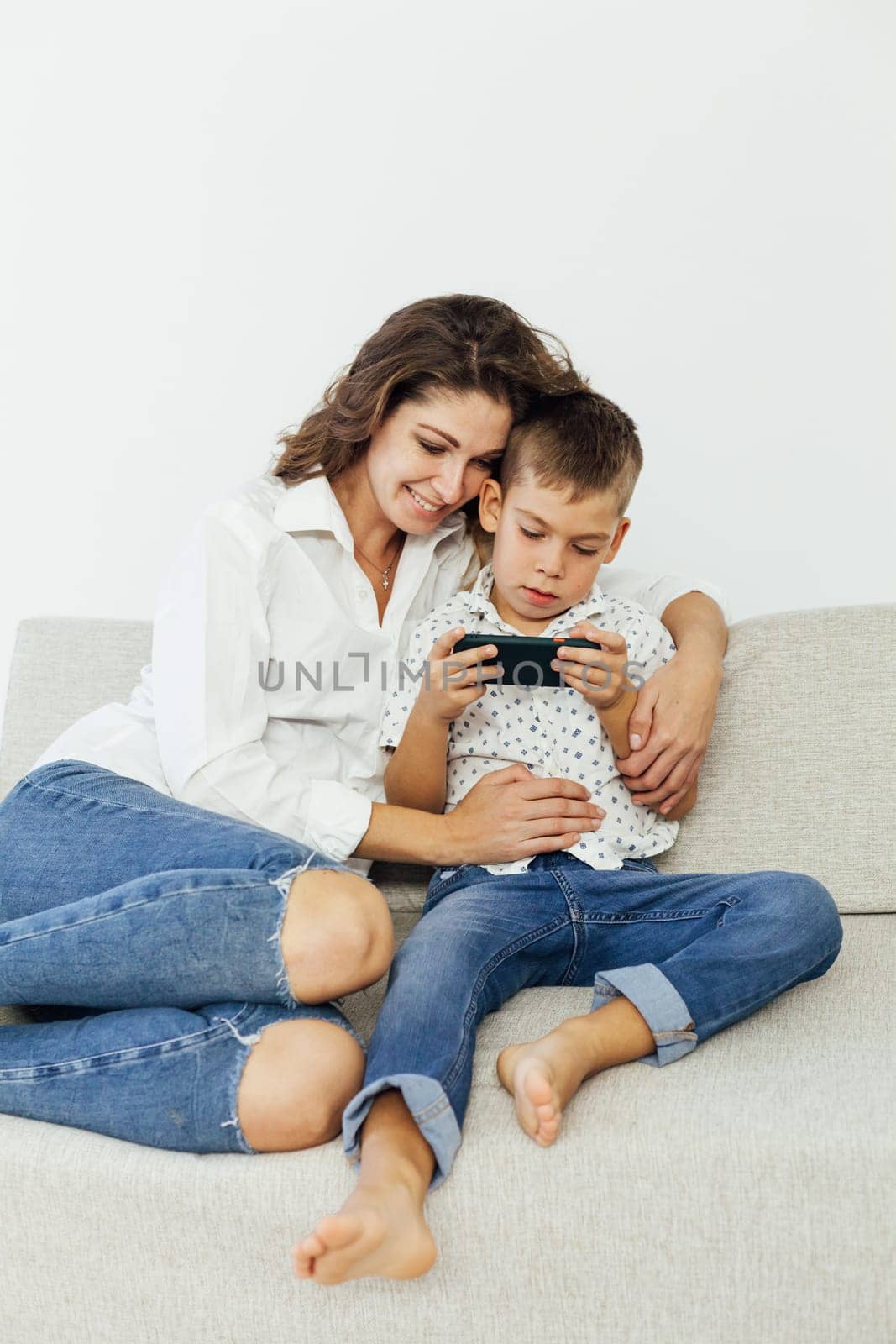 Mother and baby playing with a smart phone sitting on a couch in the living room at home by Simakov