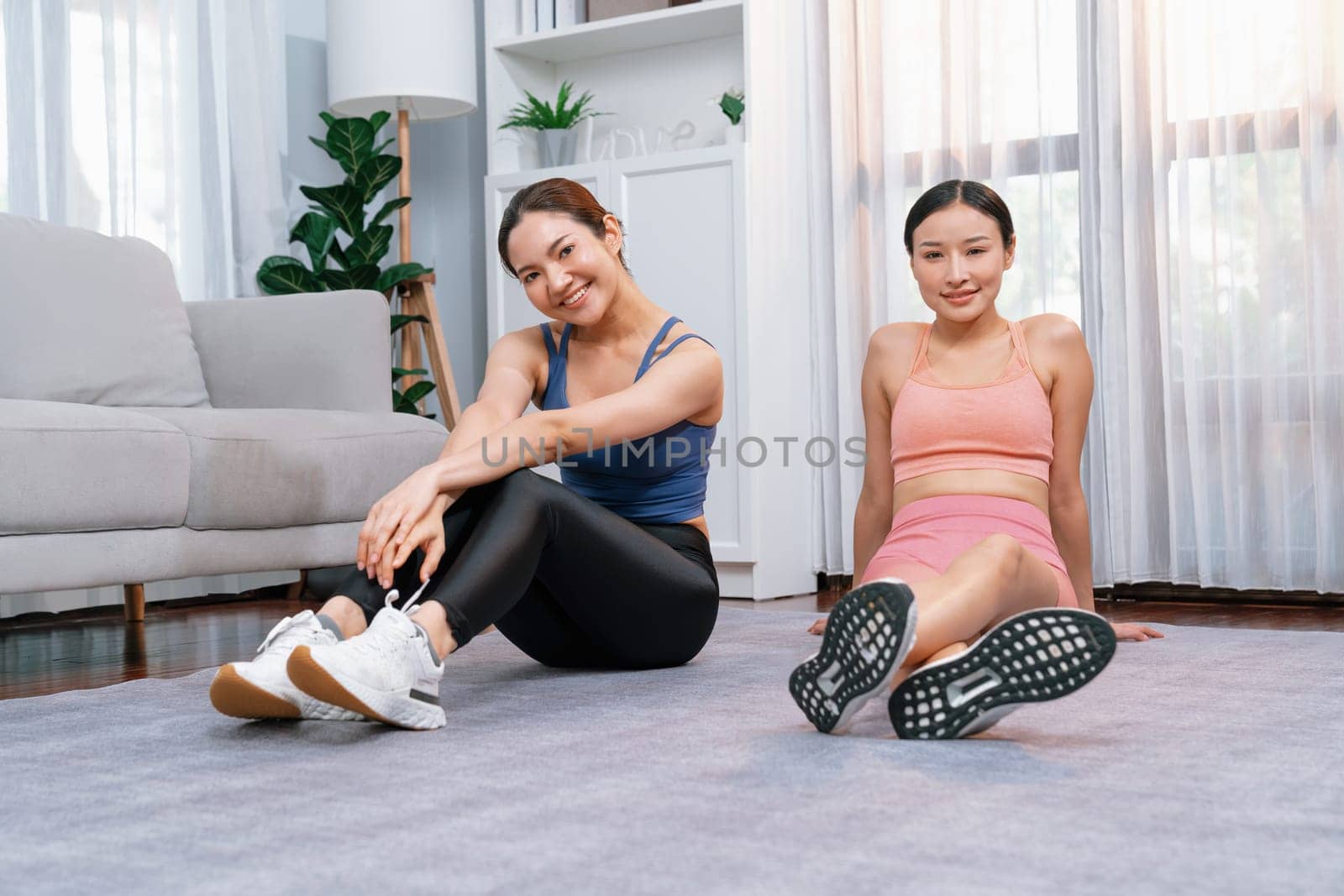 Asian woman in sportswear with her trainer or workout buddy, smiling and posing cheerful gesture. Home workout training or exercise fitness lifestyle in pursuit of healthy lifestyle. Vigorous