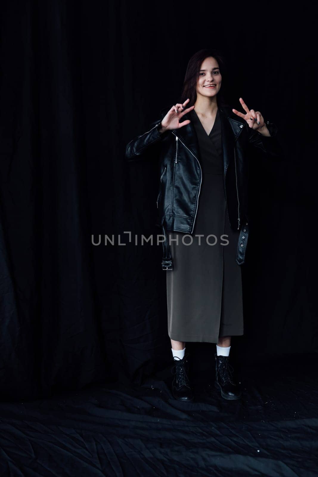 woman in dark clothes posing on a black background shows two