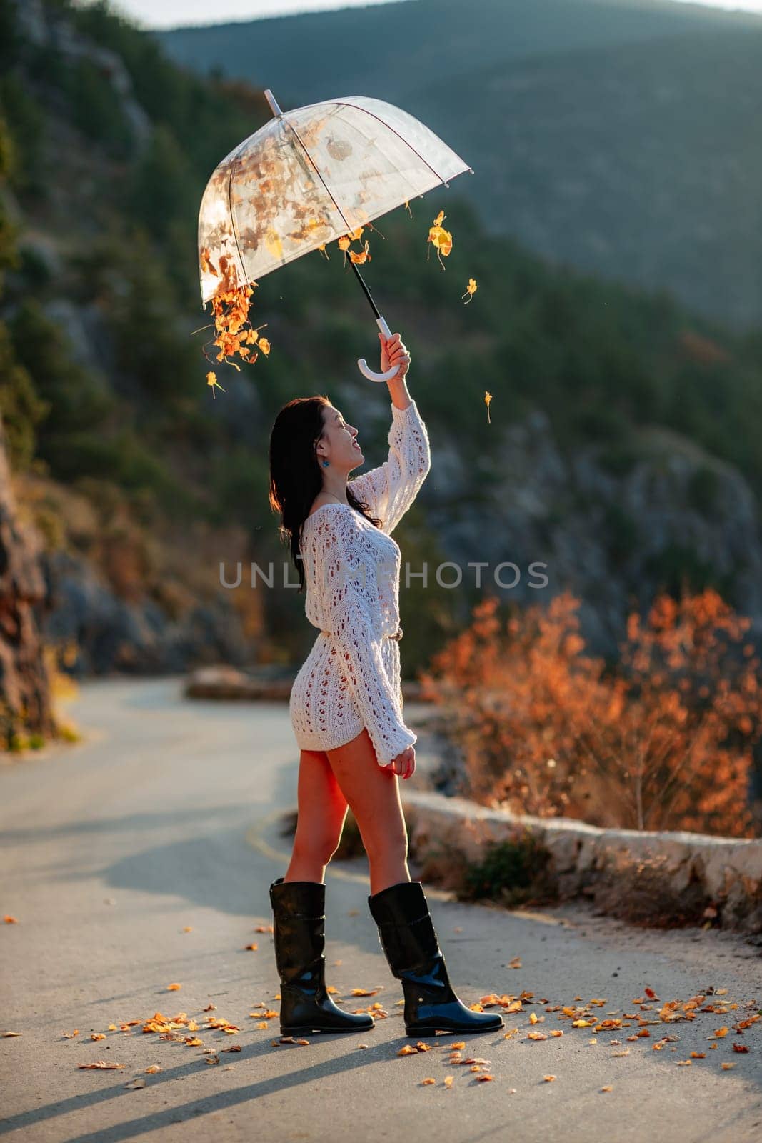 woman umbrella leaves , She holds him over her head, autumn leaves are falling out of him. Beautiful woman in a dress with an umbrella in the autumn park on the road in the mountains. by Matiunina