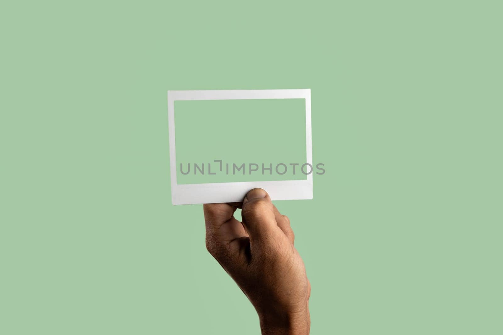 black male hand holding photo frame on isolated on light green background by TropicalNinjaStudio
