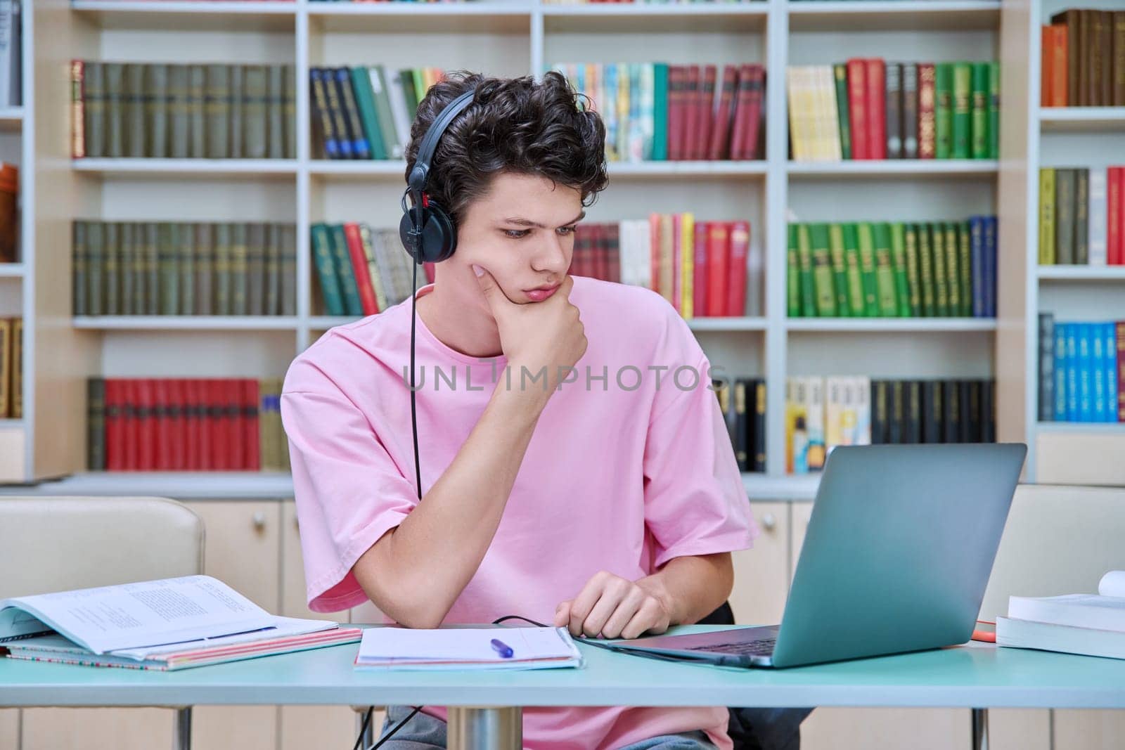 Young male student sitting with laptop with books in college library by VH-studio