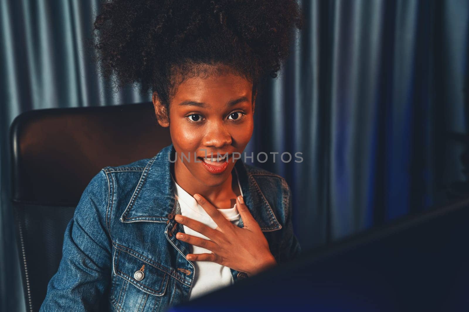 Young African American woman with surprise face, wearing blue jeans shirt and looking at final project document on laptop for planing next sequence. Concept of work at neat home place. Tastemaker.