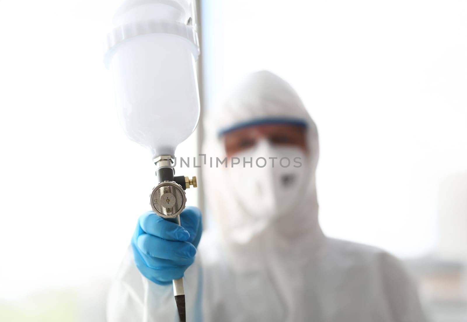Workman hold in hand sprayer wearing protective suit closeup