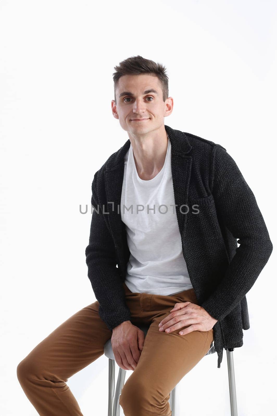 Portrait of an attractive man in a sweater and a T-shirt, sitting on a chair and smiling
