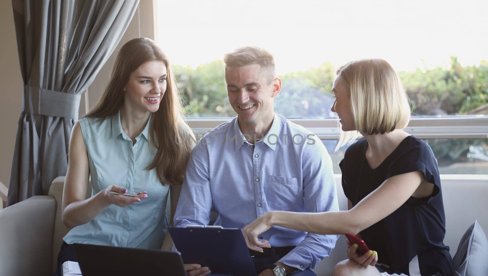 Three young business people in a cafe discussing the problem of teamwork is holding a clipboard look smiles and laughing lifestyles are examining documents and laptop.