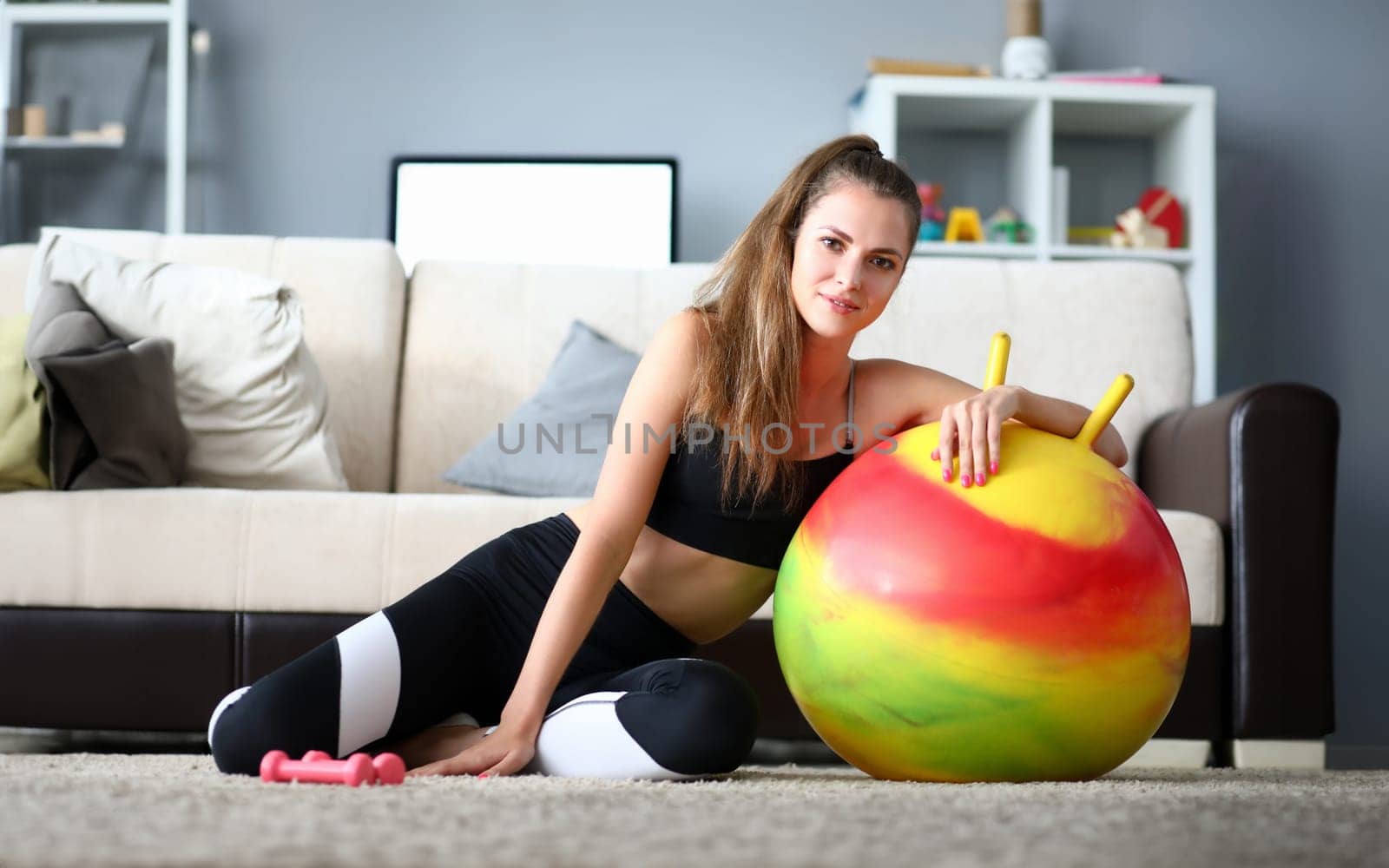 Portrait of wonderful sportswoman correcting figure with balloon and dumbbells at home. Beautiful female wearing sports suit. Fitness and sport concept