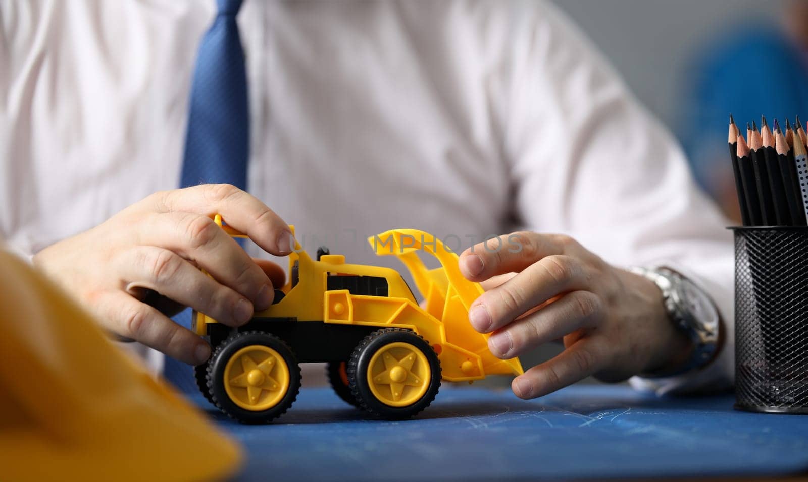 Close-up of businessman hands driving toy yellow excavator. Builder holding backhoe loader and showing future restructuring of big city. Business and construction concept
