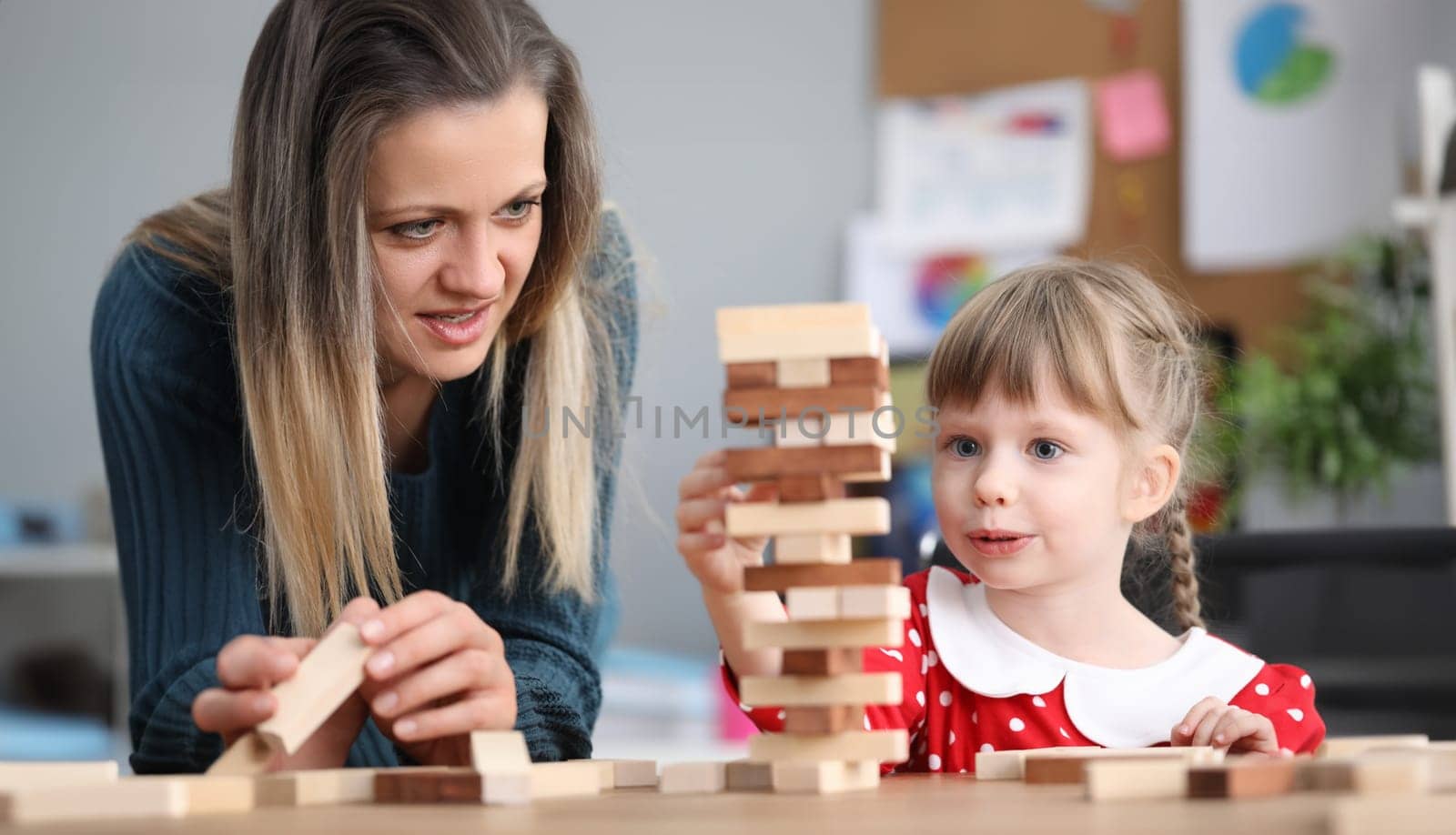 Portrait of little girl enjoying spending time with lovely mum. Thoughtful child with angel face playing with building kit. Childhood and parenthood concept