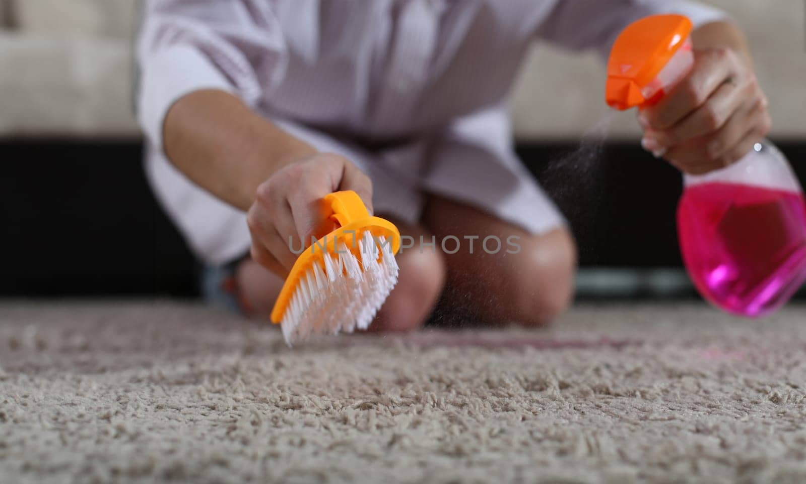 Woman holds brush and cleaning spray on carpet by kuprevich