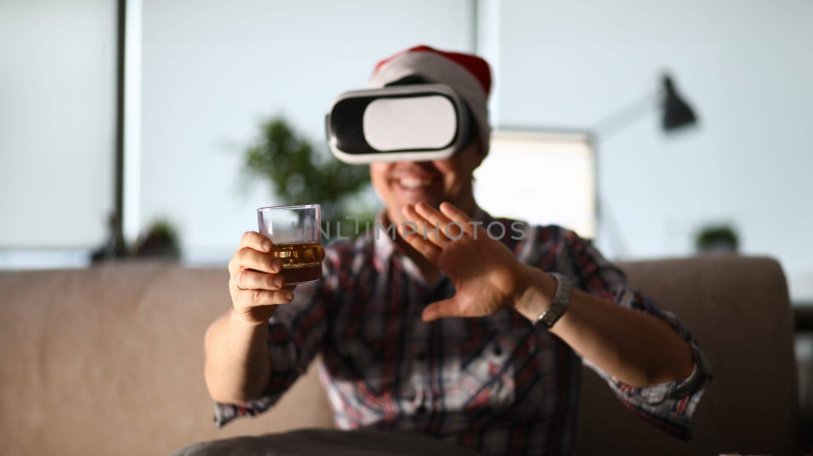 Man sit at sofa hold glass in hand and using vr gogles. Online party drinking companion concept