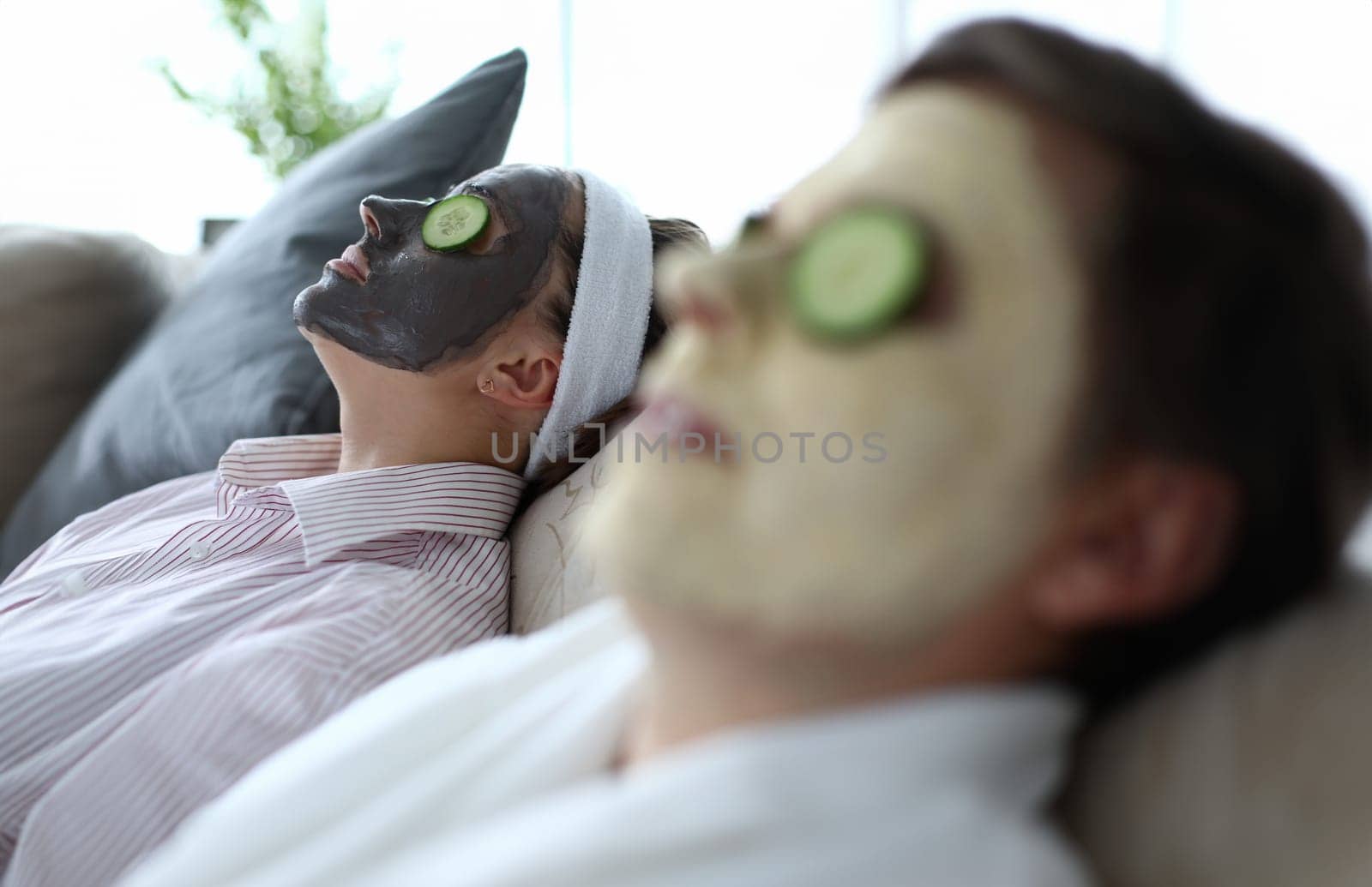 Husband and wife are lying on couch home and doing restoring face masks portrait. Healthy facial skin care at home help concept