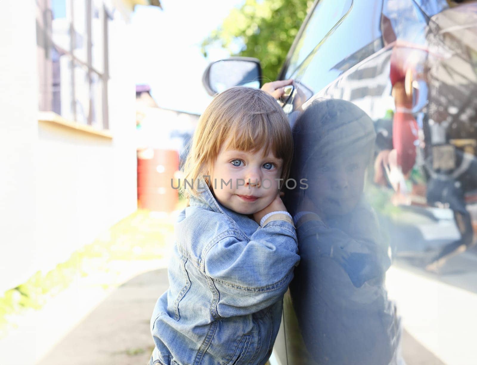 Little fashion child holds the car handle in a jeans jacket smiles and looks into the camera suitable for a fashion store