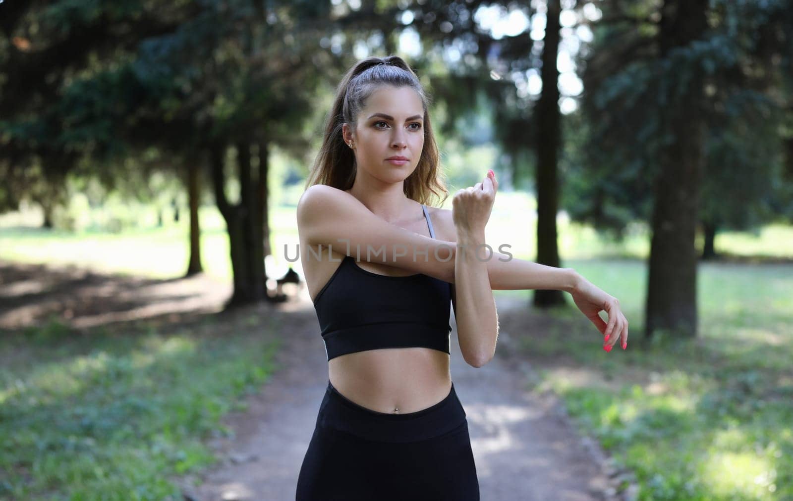 Portrait of beautiful woman correcting figure. Wonderful sportswoman doing stretching. Perfect lady with collected hair wearing sportswear. Sport and fitness concept