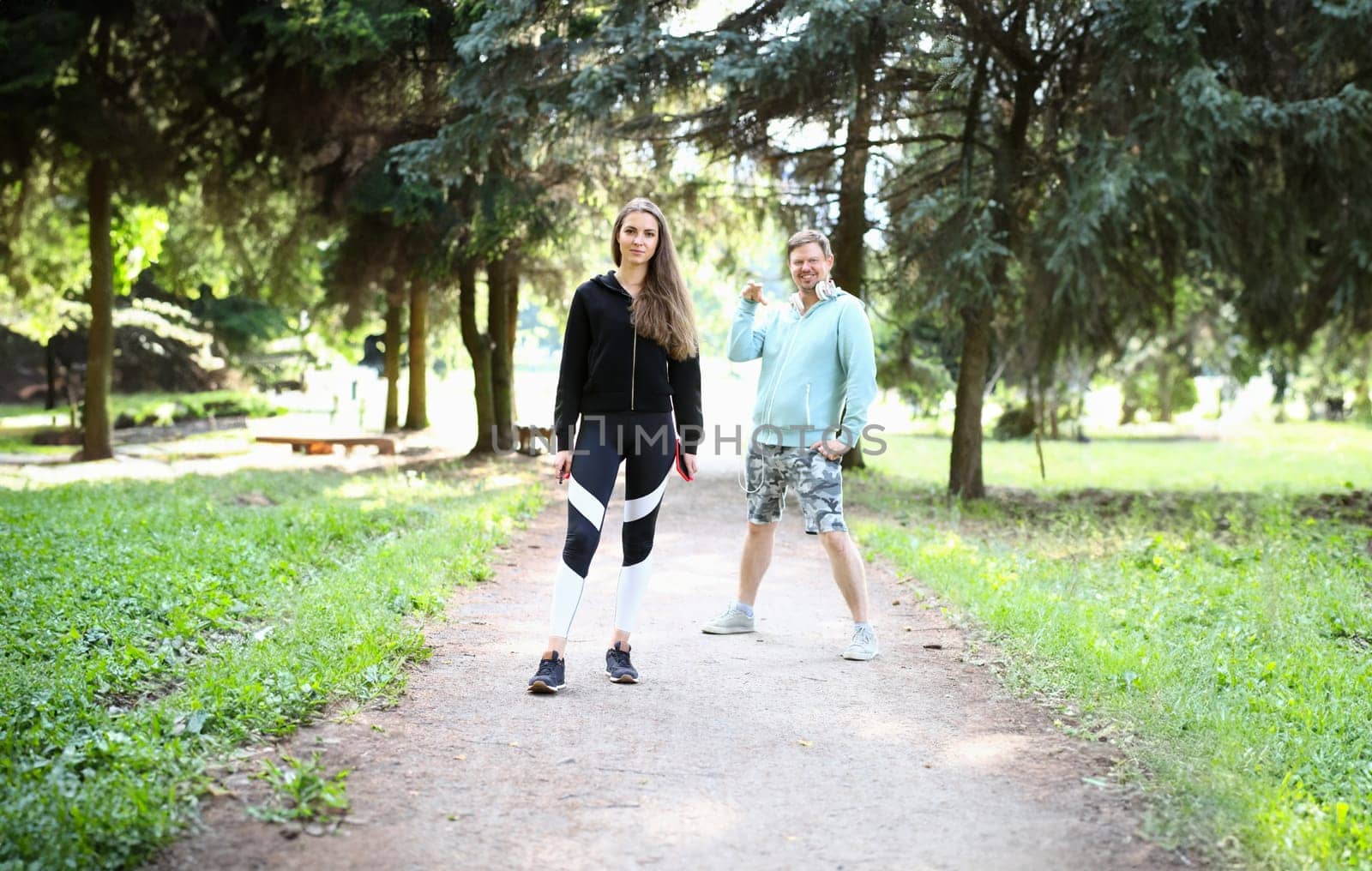 Portrait of beautiful bodybuilder and smiling man. Wonderful sportswoman wearing sportswear. Handsome boy with earphones having workout with trainer. Fitness and sport concept