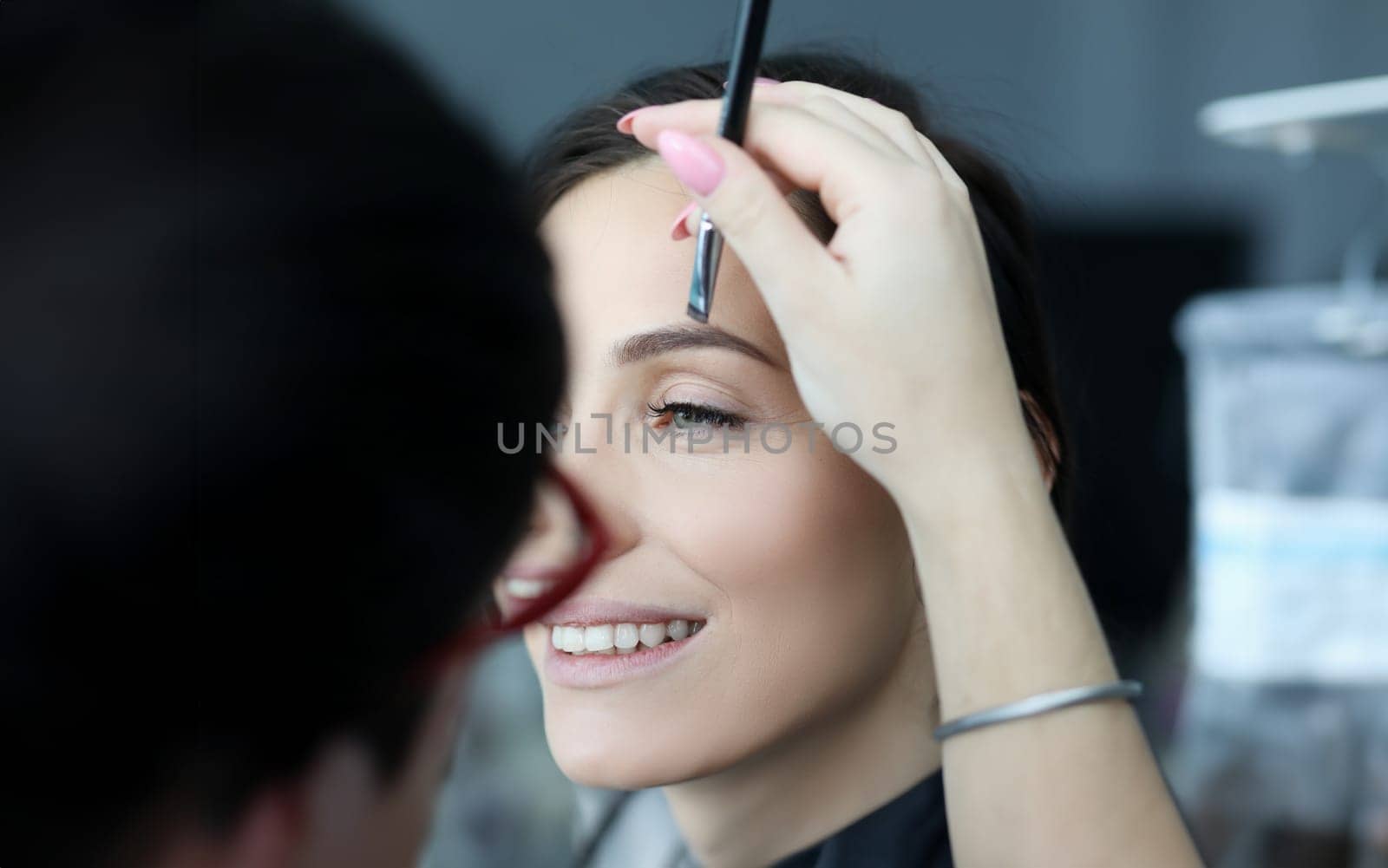 Close-up of tender female hand holding makeup professional cluster. Wonderful model looking away with happiness and smile. Beauty and cosmetics concept