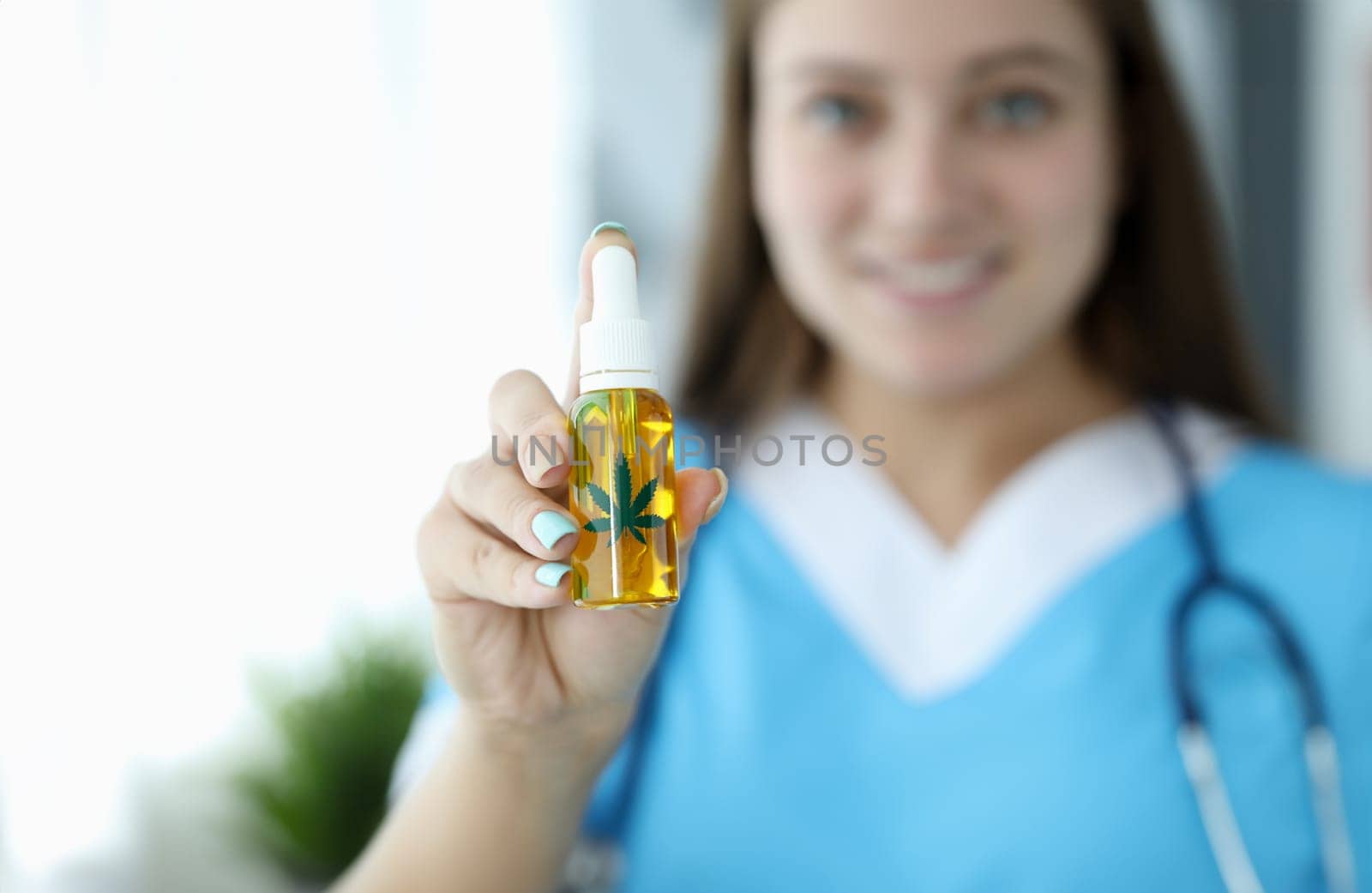 Female doctor hold in hand bottle with yellow cbd oil liquid against hospital background. Marijuana medical tratment concept