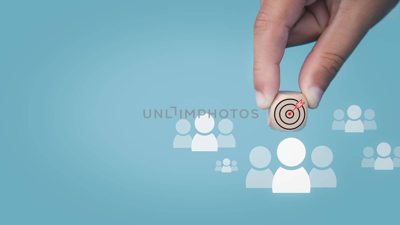 Human hand holds a dart board icon drawn on a wooden block and connects to a target customer on a light blue background It represents the selection of business goals. Marketing plans and strategies. by Unimages2527