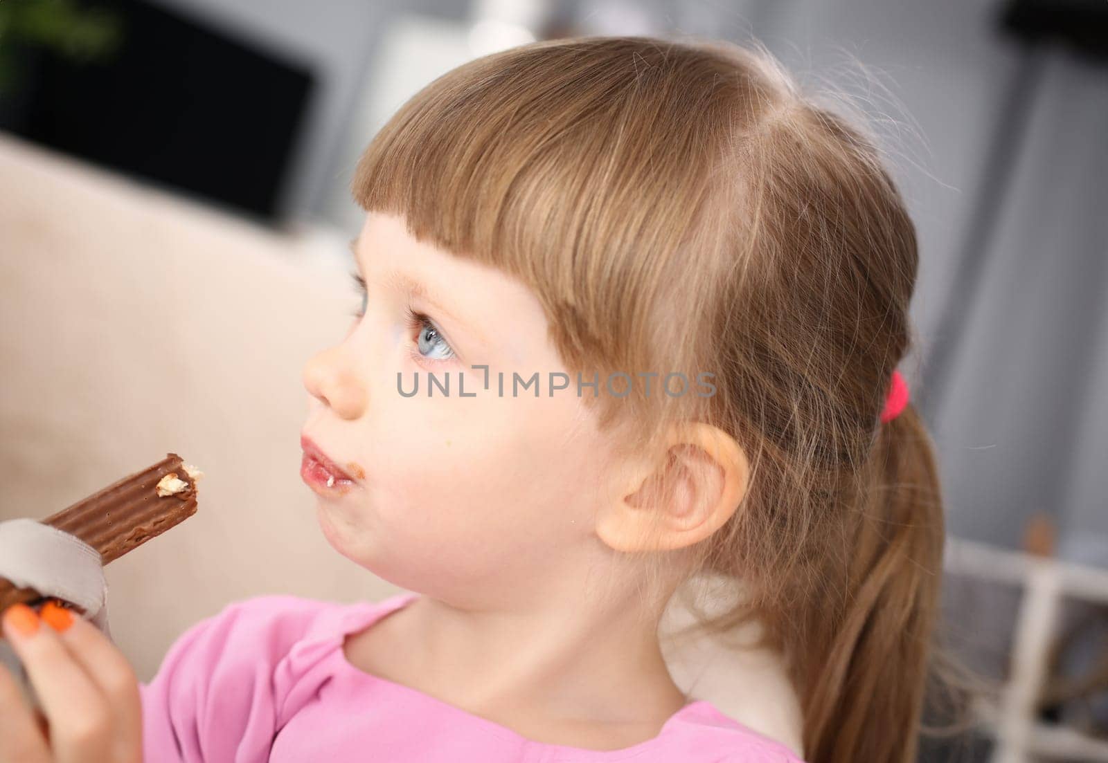 Little girl eating sweet chocolate candy with trace at her mouth by kuprevich