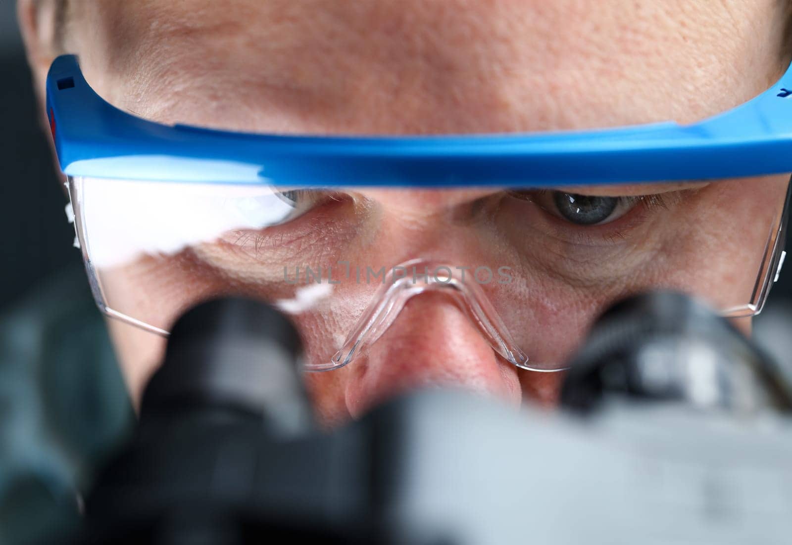 Male laboratory worker eyes looking at microscope wearing goggles closeup