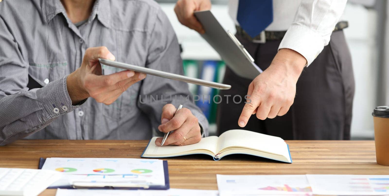 Close-up of male hands holding modern tablet and documents. Colleagues discussing important statistics data of new project and writing something in notepad. Business concept