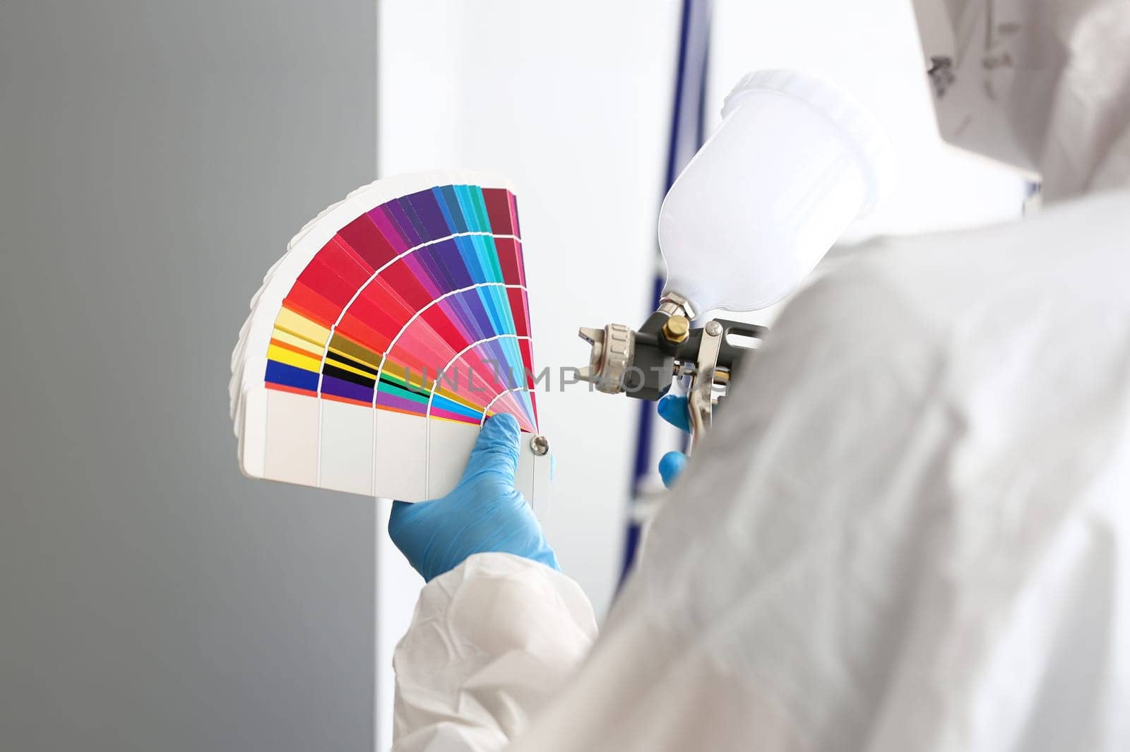 Hands of workman holding airbrush and colorful fantail picking wall tone to paint closeup